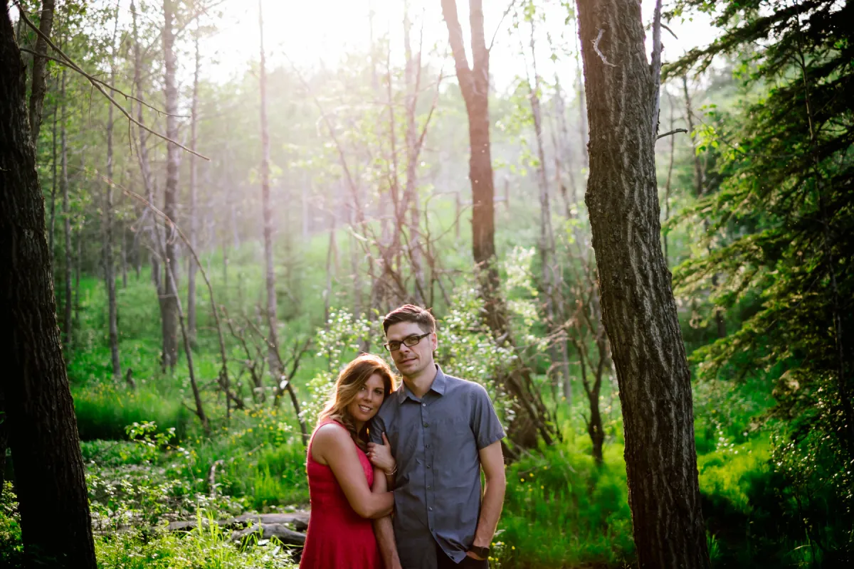Couple smiling together in sunlit pine trees during an engagement session