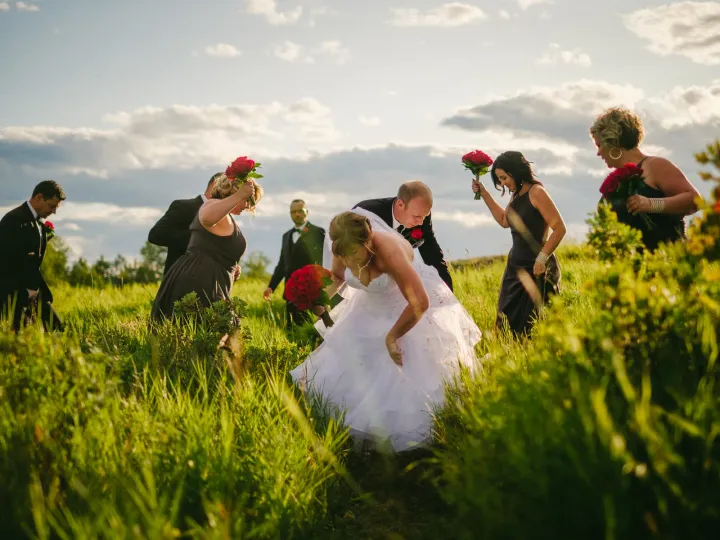 Bride, groom, and wedding party walking through tall green grass under a cloudy sky
