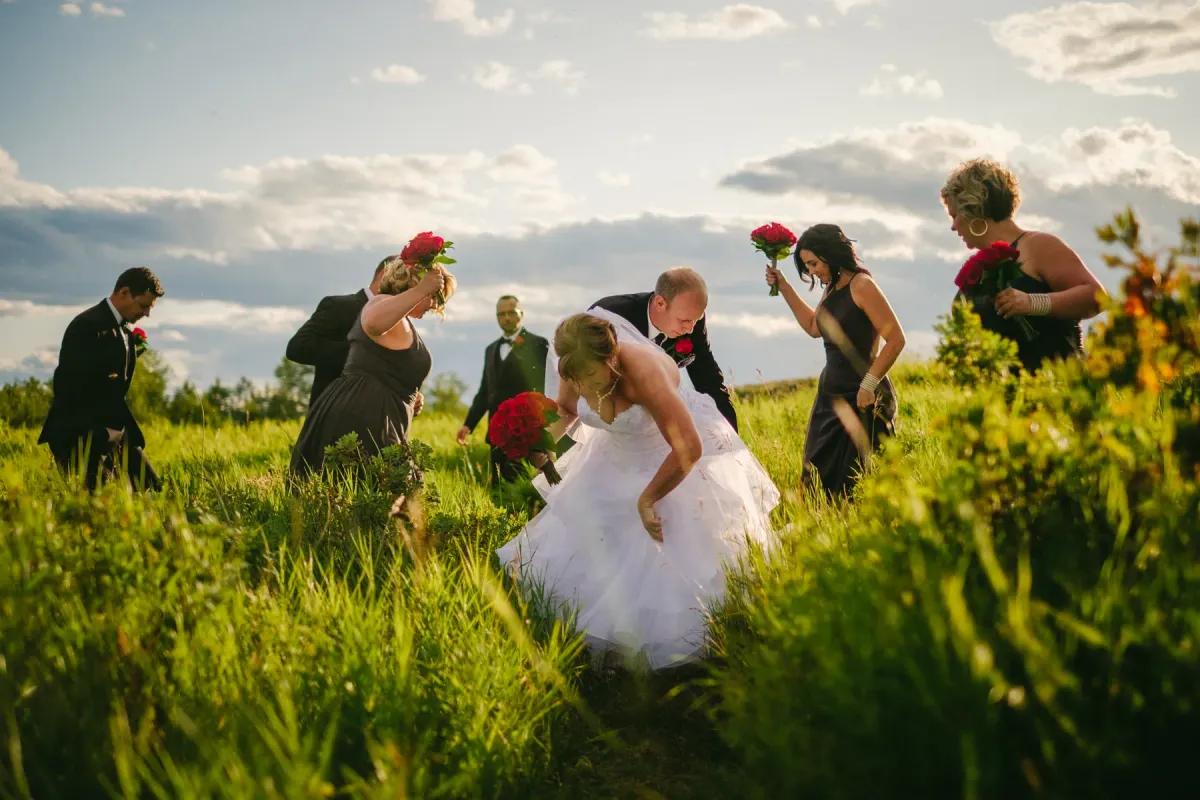 Bride, groom, and wedding party walking through tall green grass under a cloudy sky