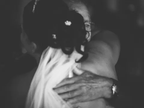 Black and white close-up of a bride hugging an older man with his hand on her back