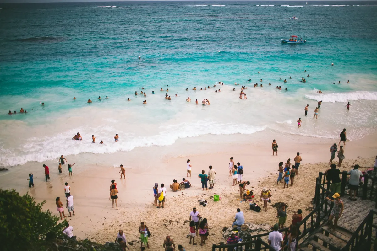 Crowded turquoise beach seen from above with swimmers along the shore