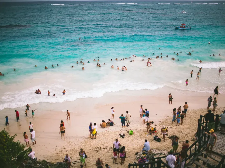 Crowded turquoise beach seen from above with swimmers along the shore
