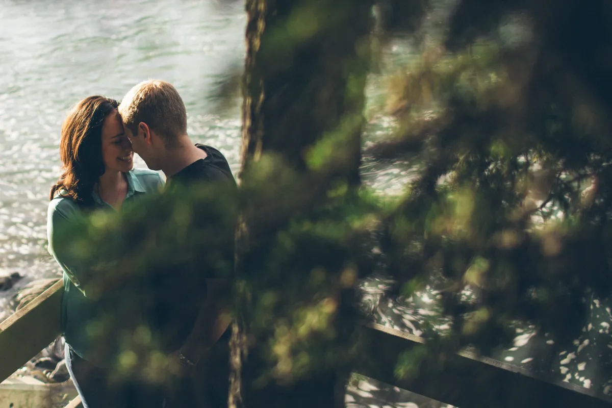 Couple smiling together through evergreen branches during an engagement session