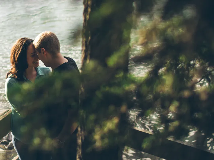 Couple smiling together through evergreen branches during an engagement session