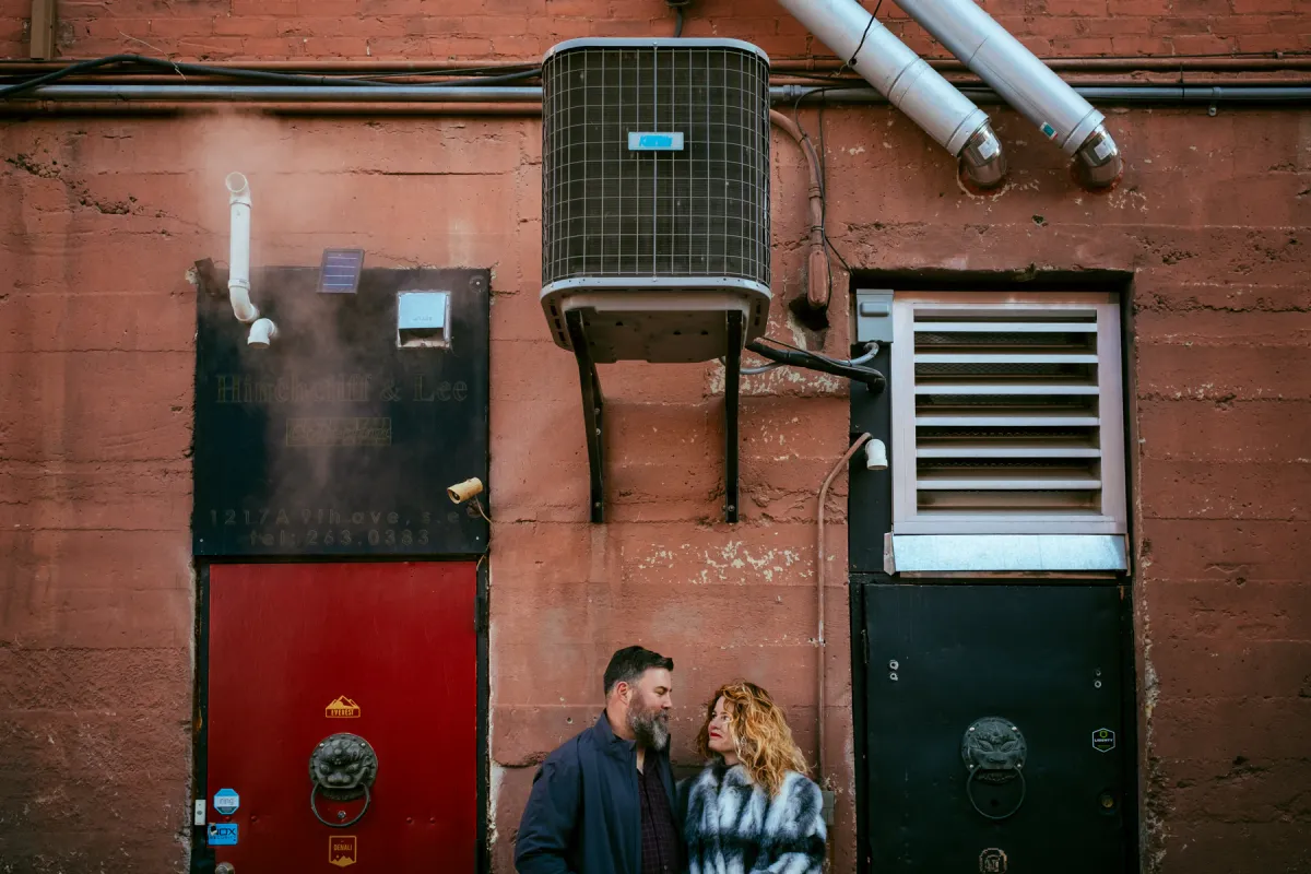 Couple standing below a red urban wall during an engagement photo session