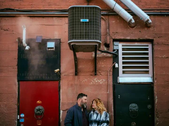 Couple standing below a red urban wall during an engagement photo session