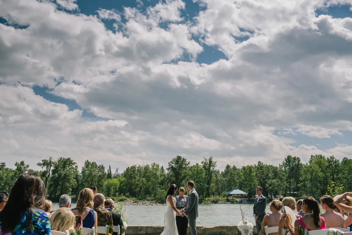 Outdoor wedding ceremony on a stone patio overlooking a river with ski jumps visible in the distance