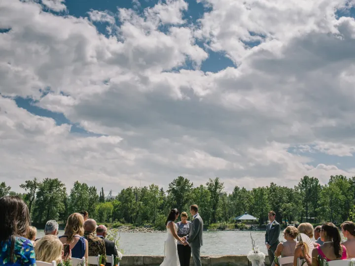 Outdoor wedding ceremony on a stone patio overlooking a river with ski jumps visible in the distance