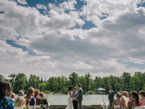 Outdoor wedding ceremony on a stone patio overlooking a river with ski jumps visible in the distance
