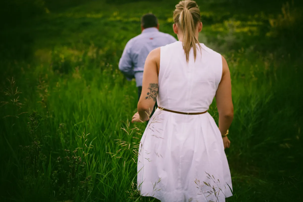 Couple walking away through tall green grass during an Alberta engagement session