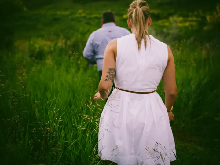 Couple walking away through tall green grass during an Alberta engagement session