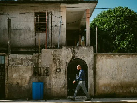 Person walking past a concrete wall with a dark arched doorway