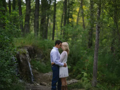 Engaged couple standing together near a small forest waterfall