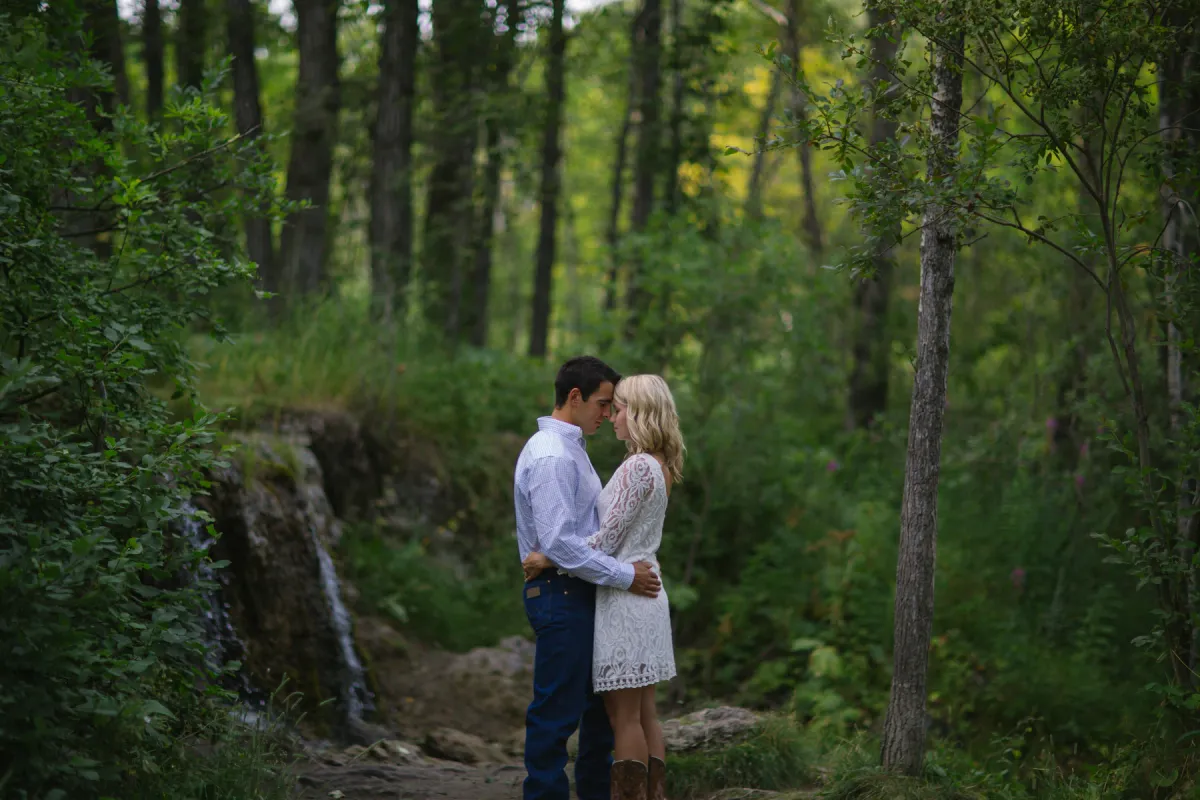 Engaged couple standing together near a small forest waterfall