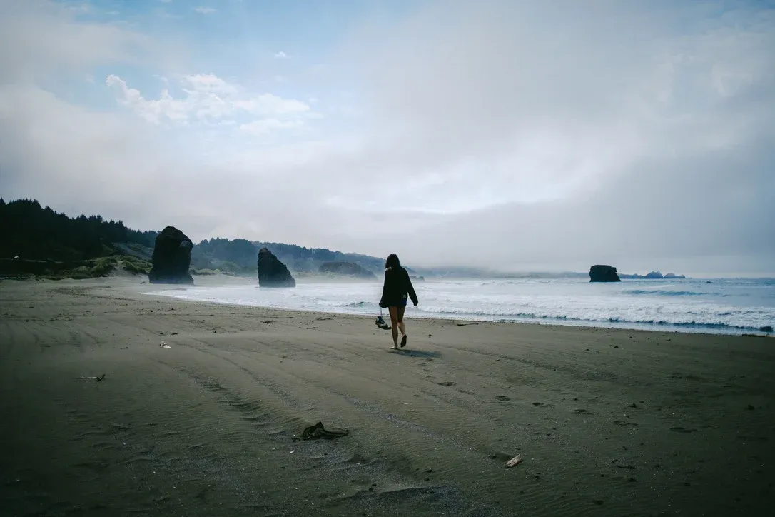 Person walking along a grey beach under heavy coastal weather
