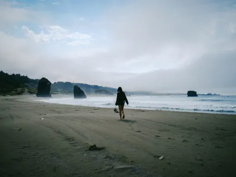 Person walking along a grey beach under heavy coastal weather