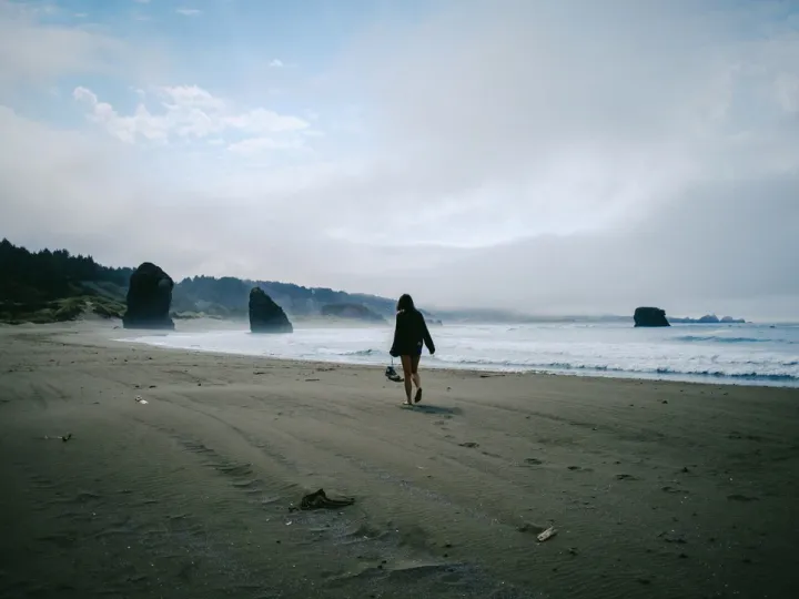 Person walking along a grey beach under heavy coastal weather