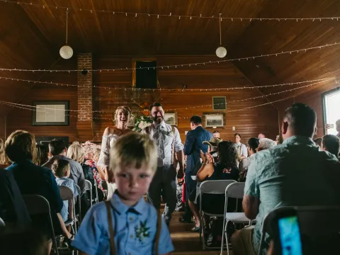 Bride and groom laughing while walking down a wood-paneled aisle with a young boy ahead