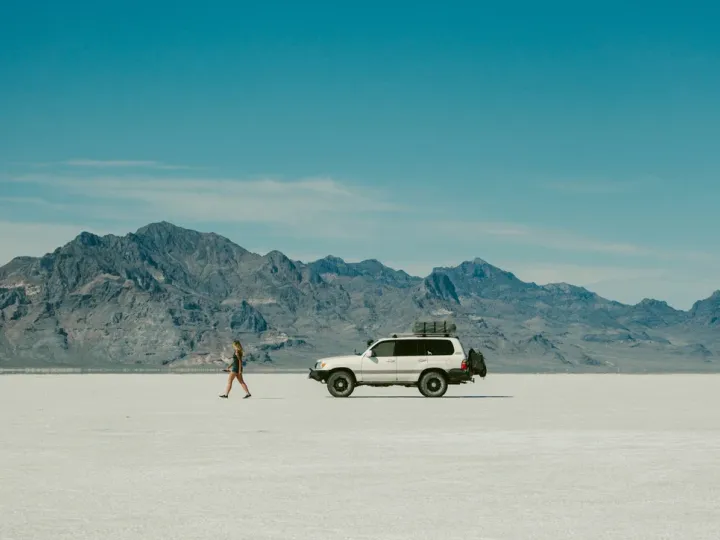White vehicle parked on pale desert ground beneath mountains