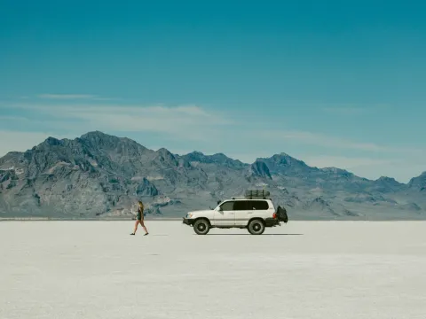 White vehicle parked on pale desert ground beneath mountains