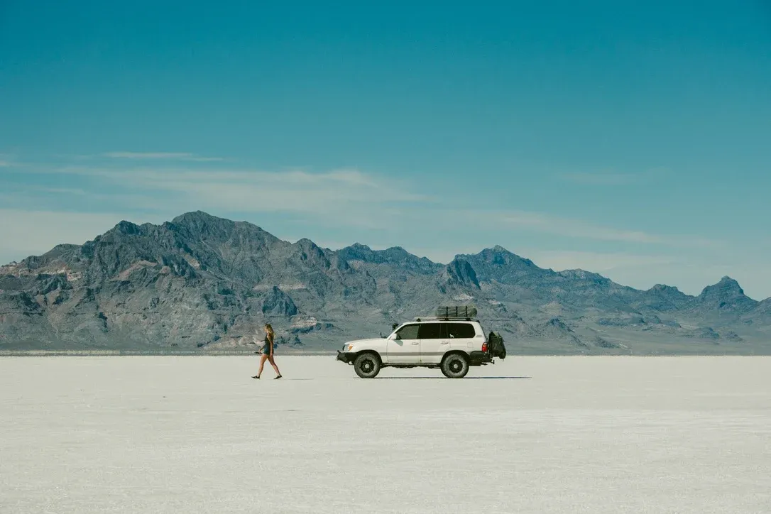 White vehicle parked on pale desert ground beneath mountains
