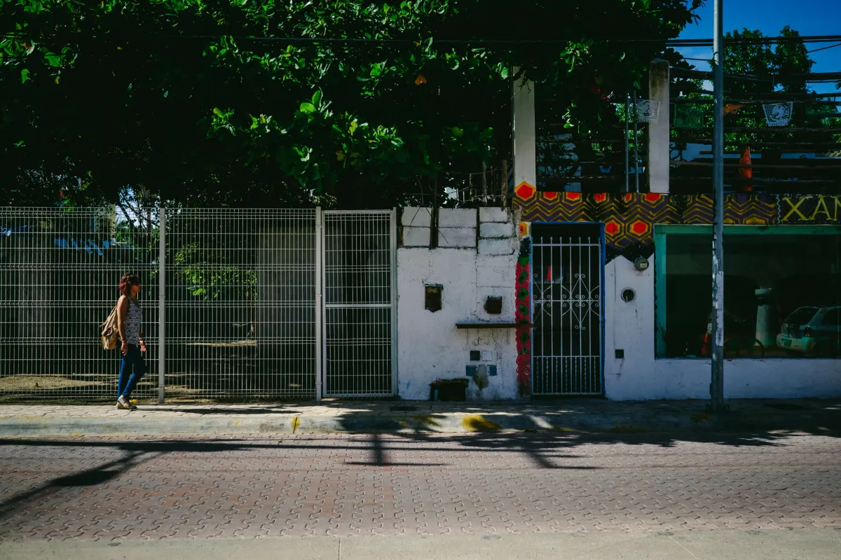 Person walking past a white wall and gate in strong afternoon sunlight