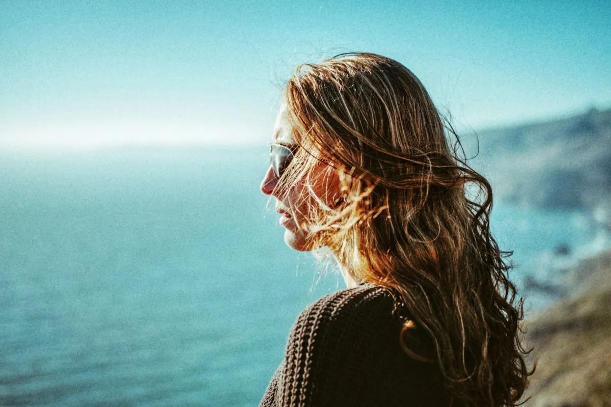 Close coastal portrait of a woman with windblown hair and blue water behind her