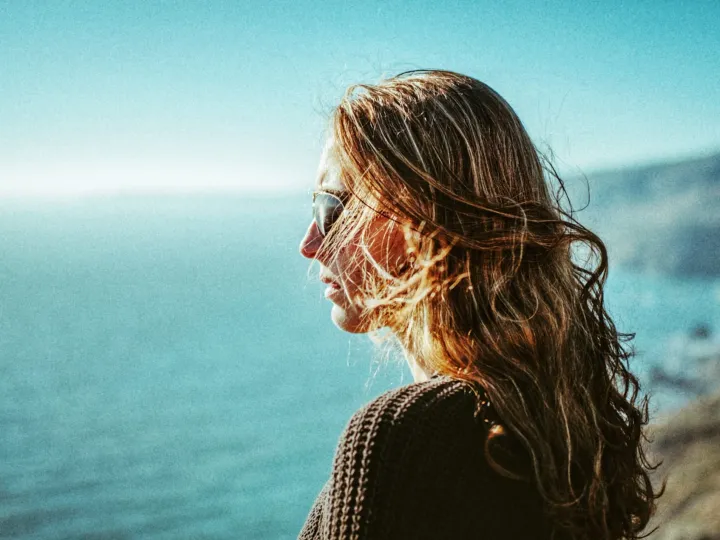 Close coastal portrait of a woman with windblown hair and blue water behind her